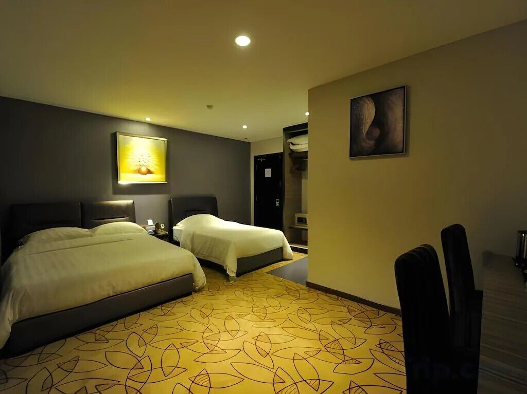 A hotel room with two beds, a desk, and a chair. There is a painting on the wall and a lamp on the desk.