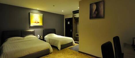 A hotel room with two beds, a desk, and a chair. There is a painting on the wall and a lamp on the desk.