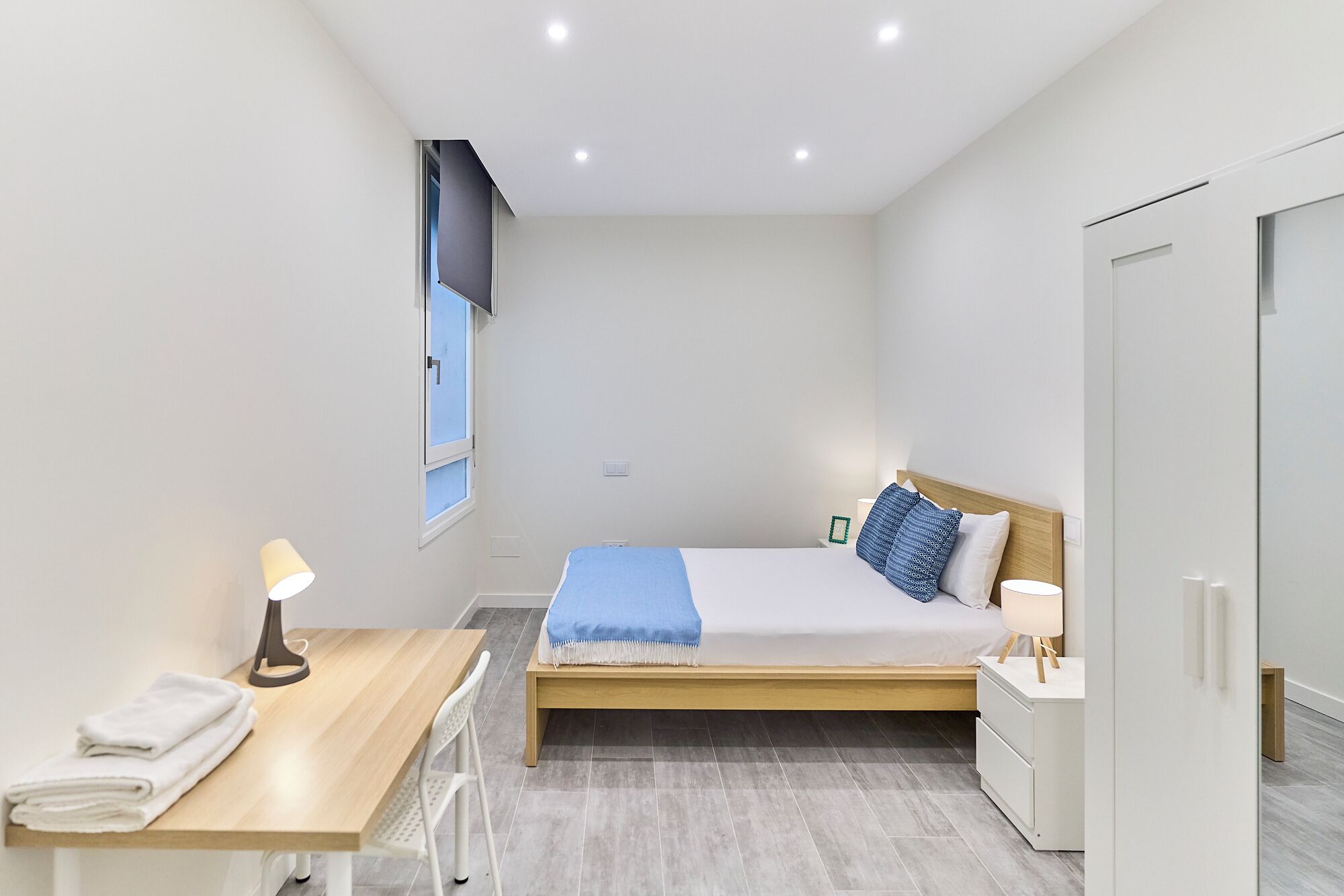 Een moderne slaapkamer met een bed, nachtkastje, lamp en een bureau met stoel.