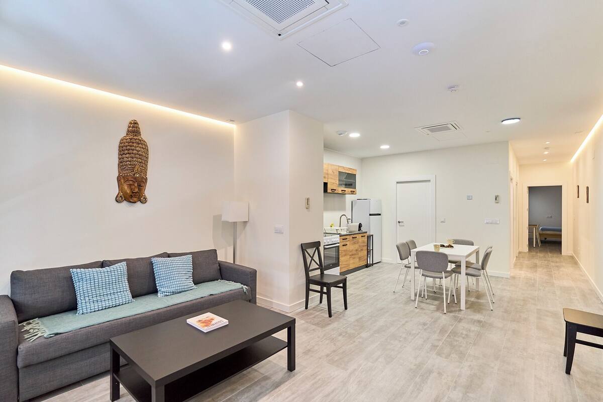 Eine moderne Wohnung mit Wohnbereich, inklusive Sofa, Couchtisch und Esstisch mit Stühlen. Es gibt eine Küchenzeile mit Kühlschrank und Herd.