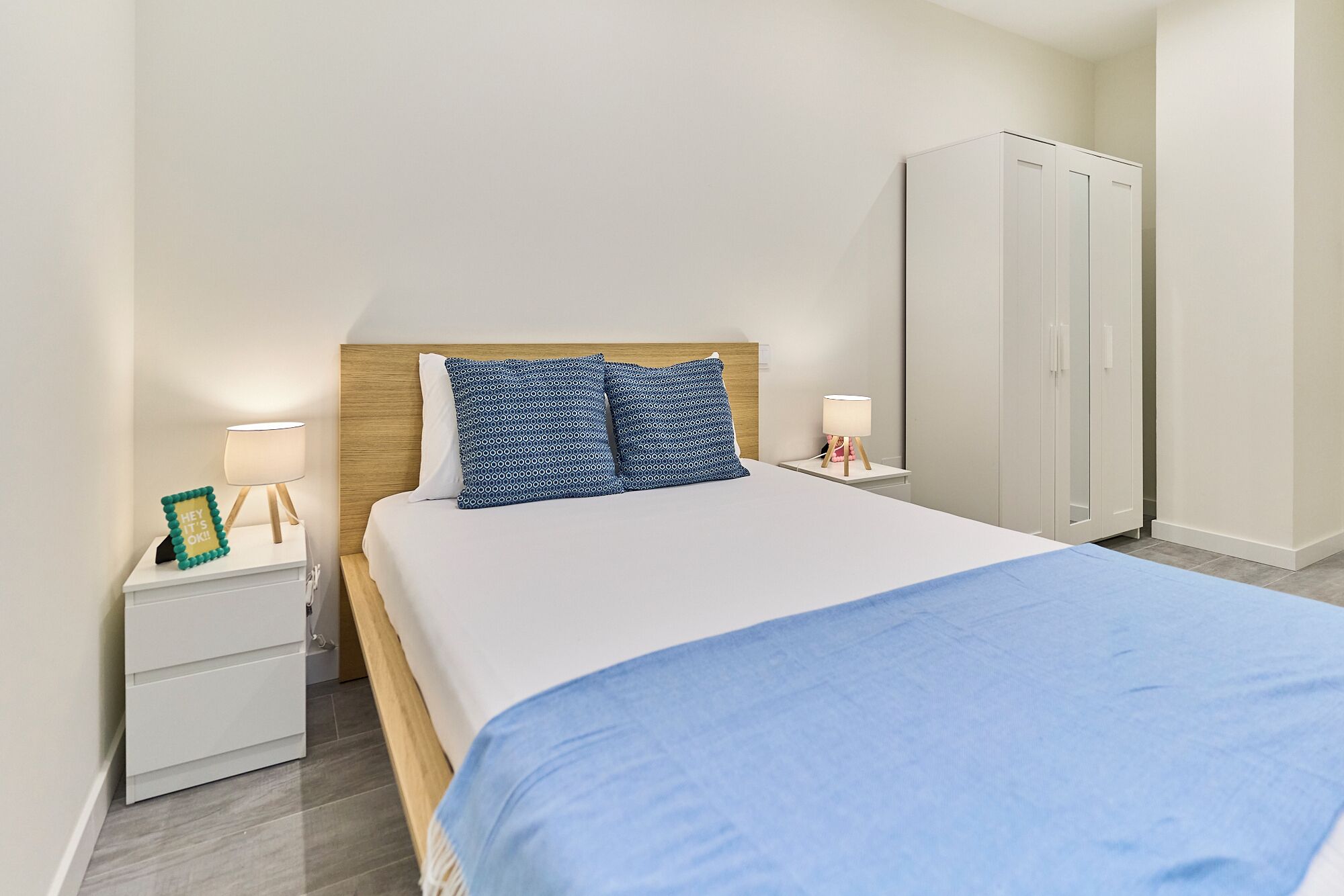 Een keurig opgemaakt slaapkamer met een bed, nachtkastjes, een kledingkast en een bedlampje.
