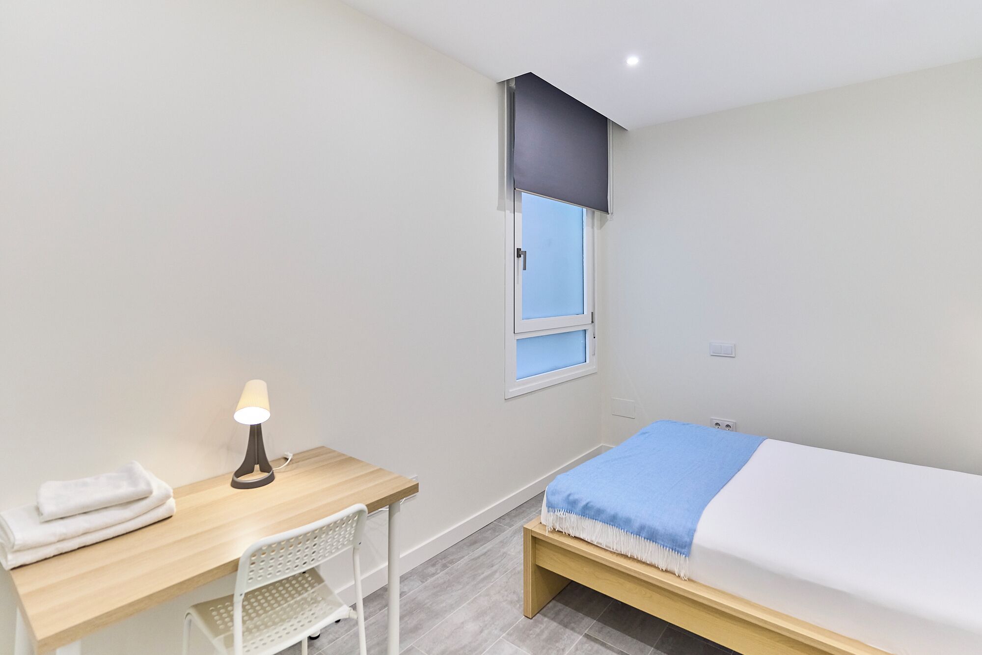 A small, clean room with a bed, a desk, and a chair.