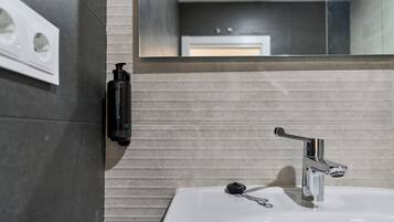A bathroom with a white sink, a chrome faucet, and a soap dispenser on the wall.