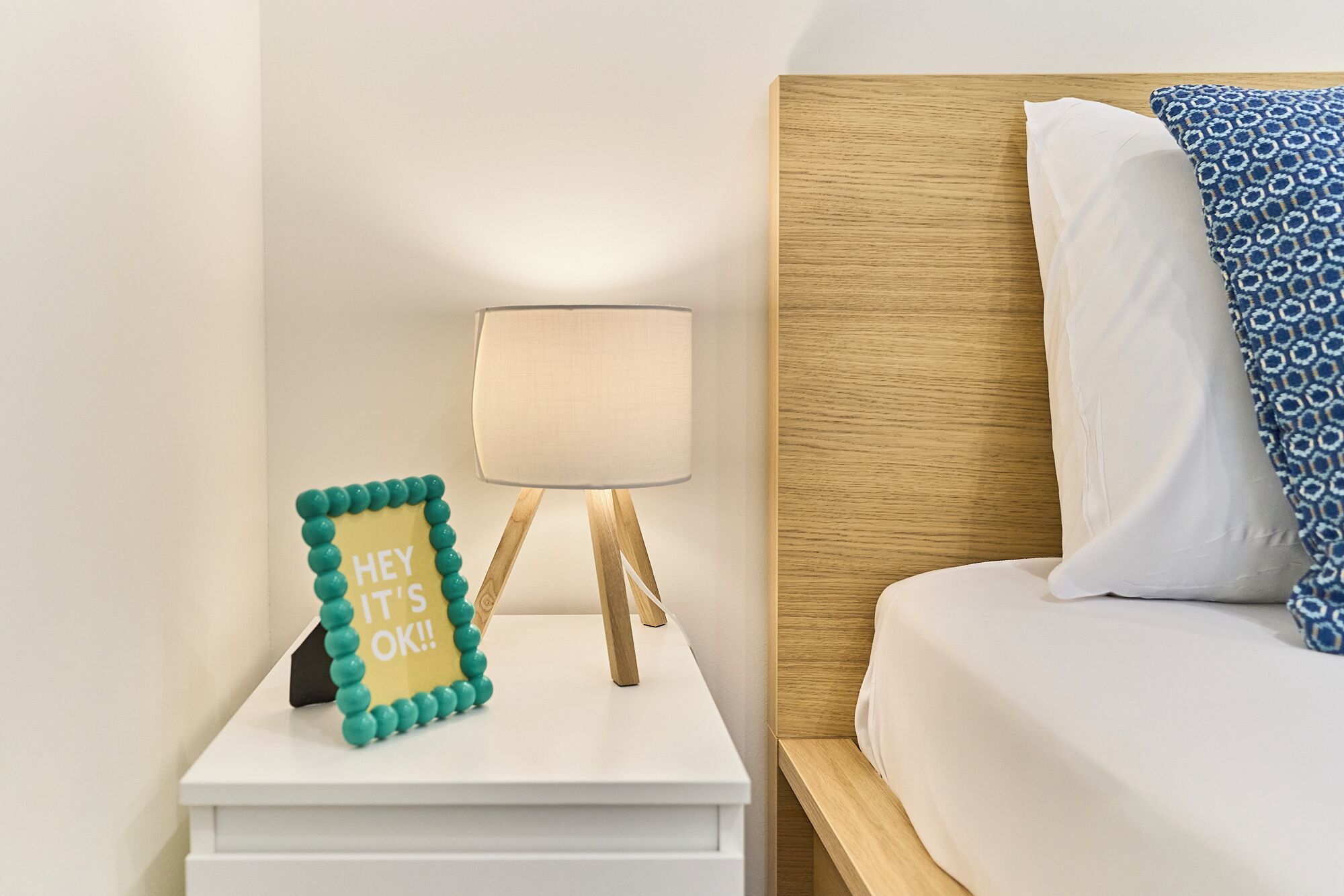 A neatly made bed with a patterned pillow, a bedside lamp, and a decorative sign on the nightstand.