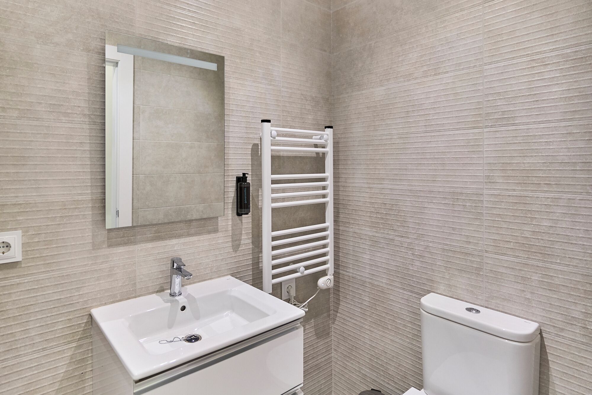 Een badkamer met een witte wastafel, een spiegel, een handdoekhouder en een toilet.