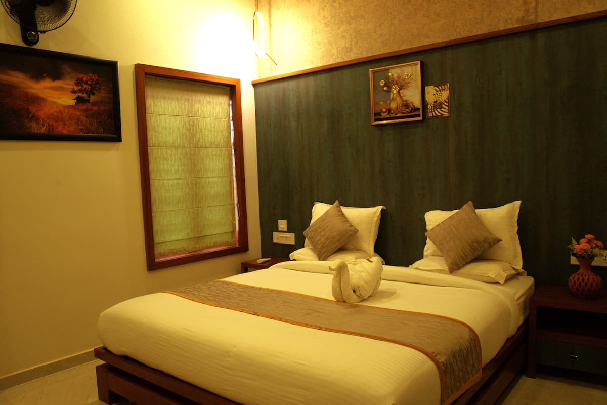 A hotel room with a large bed, a nightstand, a vase with flowers, and a painting on the wall.