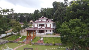A large, two-story house with a tiled roof, surrounded by lush greenery and a well-maintained garden. - Tatvaura Resort Wayanad (Vythiri)