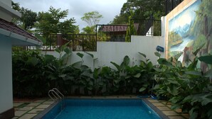 A swimming pool surrounded by lush greenery and a mural. - Tatvaura Resort Wayanad (Vythiri)