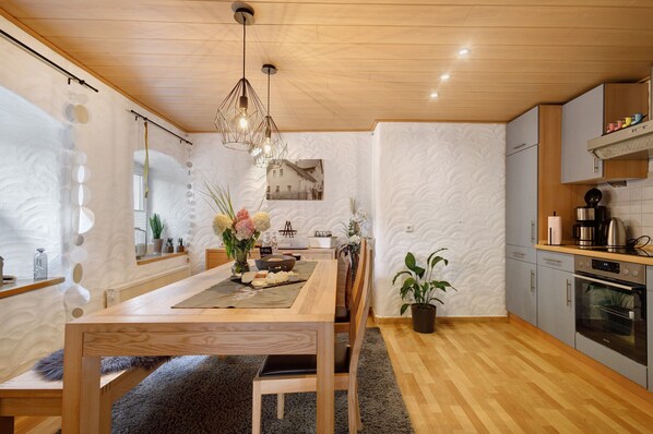 A modern kitchen with wooden cabinets, a built-in oven, and a dining area with a wooden table and chairs.