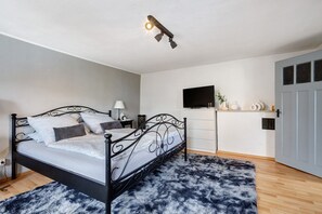 A bedroom with a bed, bedside table, lamp, TV, and a door.