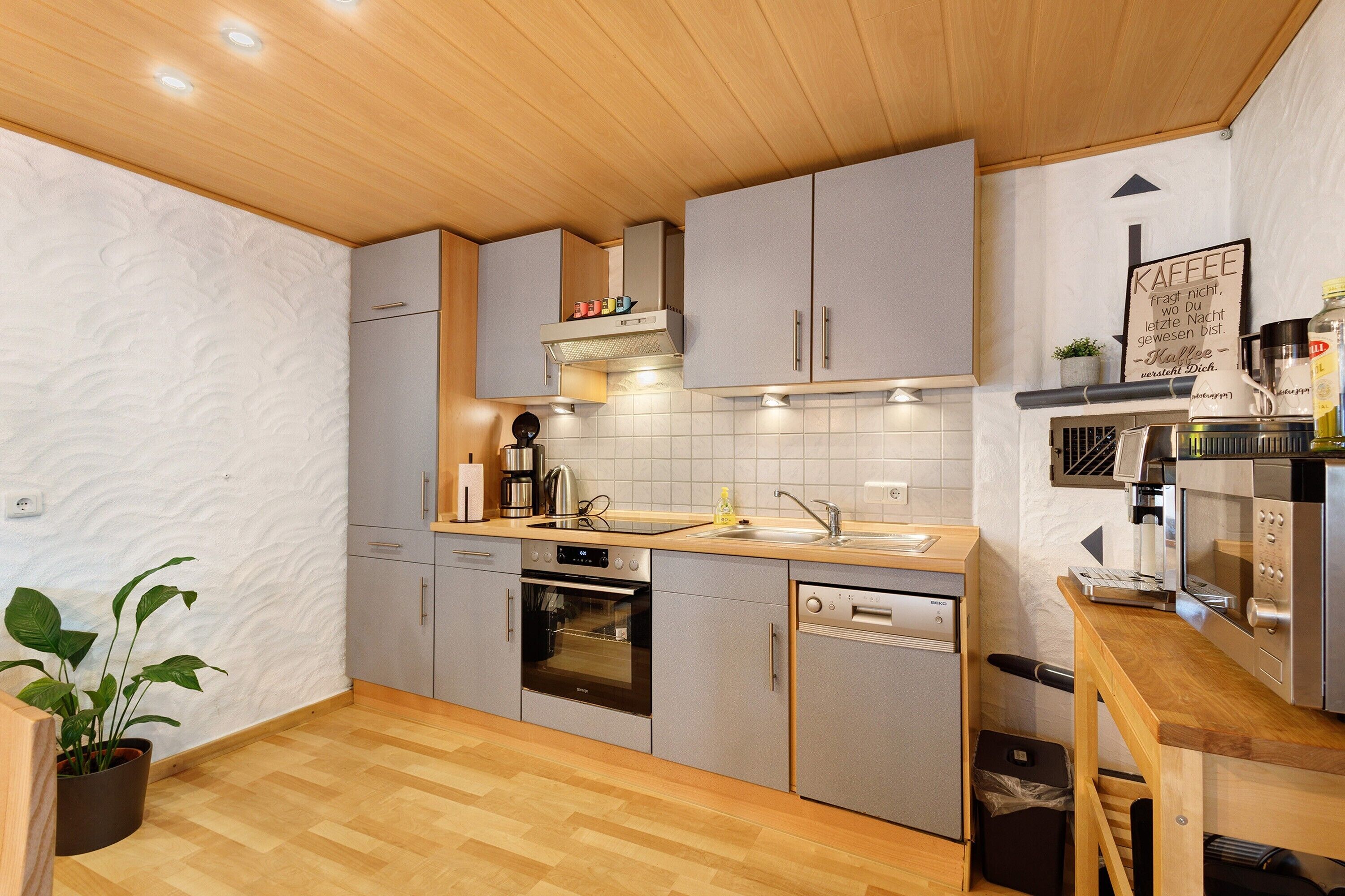 A modern kitchen with grey cabinets, a wooden countertop, and stainless steel appliances including a dishwasher, oven, and microwave.