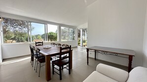 A dining area with a wooden table and chairs, large windows with a view of trees, and a small table with a white cushion. - Casa do Monte by Check-in Portugal (Albufeira)