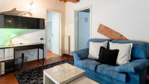 A living room with a blue sofa, a desk with a lamp, and a radiator. - GuestHost - Venezia Nuova Apartment Livorno (Livorno)