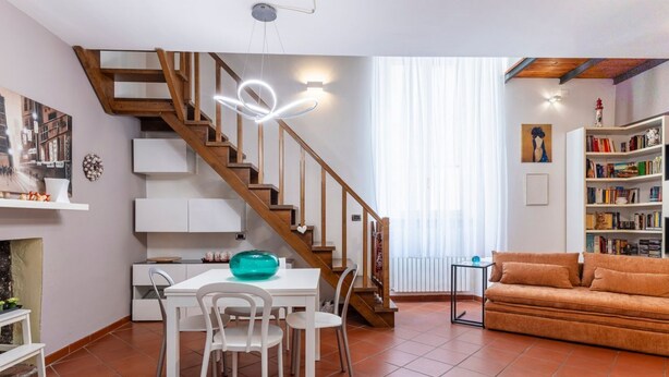 A living room with a staircase, a dining table with chairs, a sofa, and a bookshelf. - GuestHost - Venezia Nuova Apartment Livorno (Livorno)