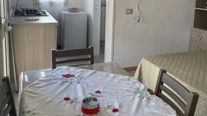 Una habitación compacta con cama, kitchenette pequeña, televisor montado en la pared y ventana que proporciona luz natural.