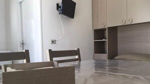 Una habitación con una mesa de madera, sillas, un televisor montado en la pared y estanterías empotradas.