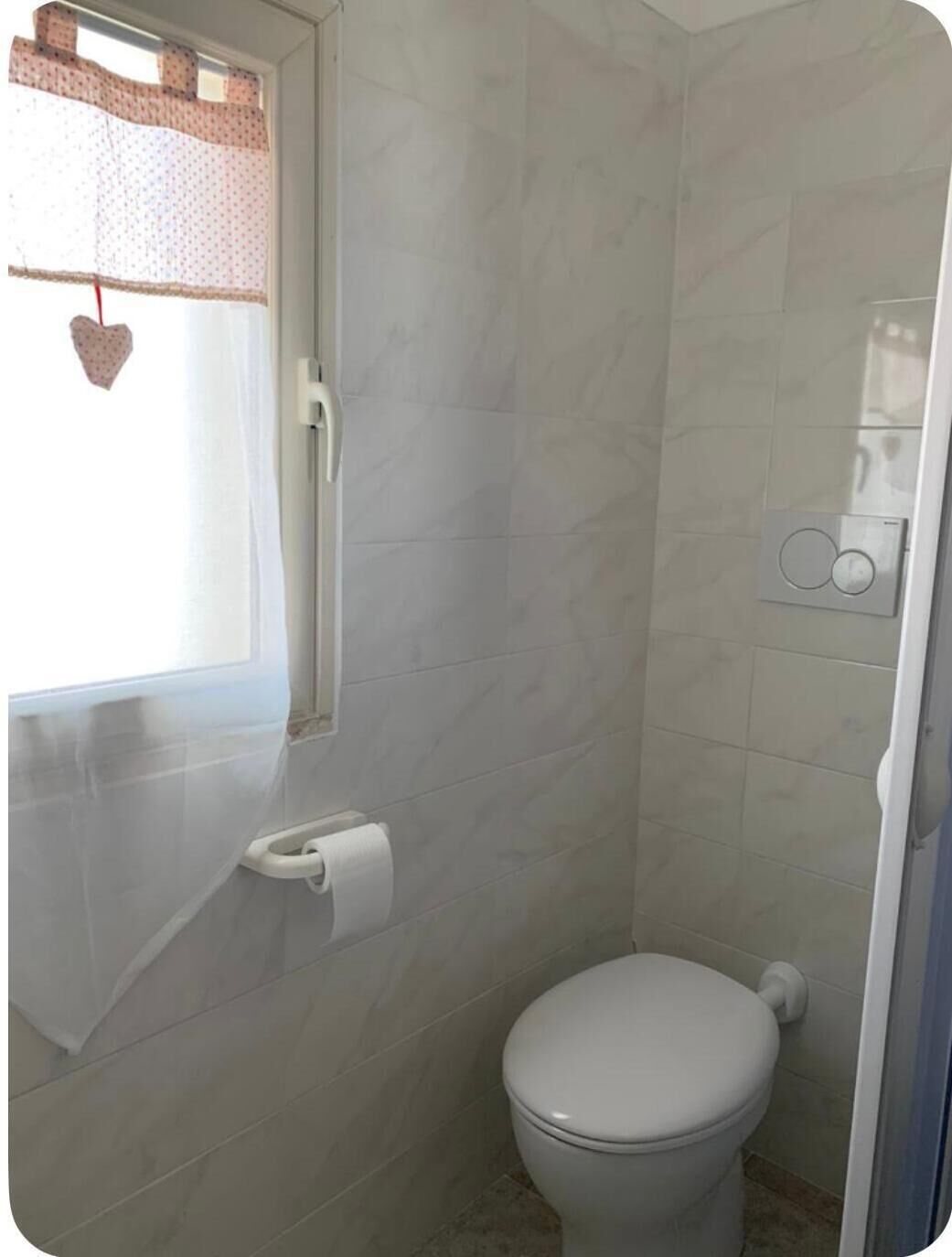 Een badkamer met toilet, douche en raam met decoratie in de vorm van een hart.