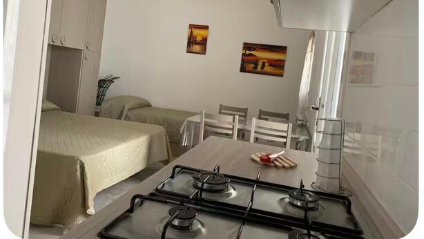 Una habitación compacta con una cama, una pequeña mesa con sillas, una estufa a gas y dos cuadros colgados en la pared.