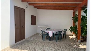 Un porche cubierto con piso de piedra, una mesa redonda con sillas y una pérgola de madera.
