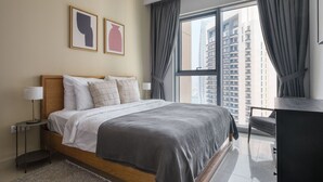A modern hotel room with a large bed, a nightstand, a lamp, and a view of tall buildings through the window.