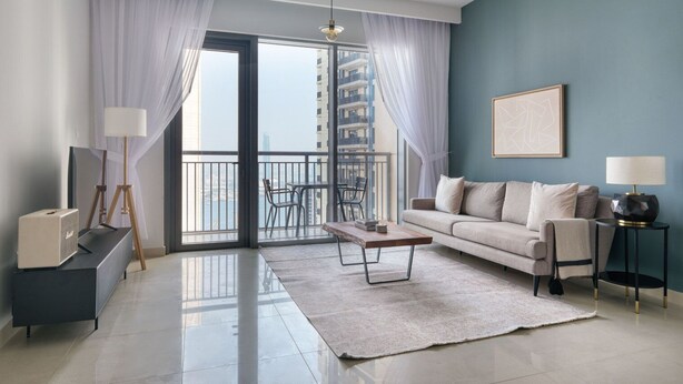A modern living room with a sofa, coffee table, and a view of a cityscape through large windows.