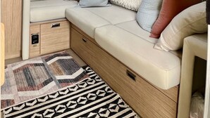A cozy RV interior with a cushioned seating area, a patterned rug, and a window offering a view of greenery. - “Moonbeam” (Airstream) (Oakland)