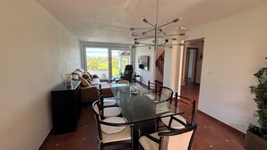 Un comedor amplio con mesa y sillas de vidrio, una lámpara moderna y vistas a un área exterior a través de puertas correderas grandes.