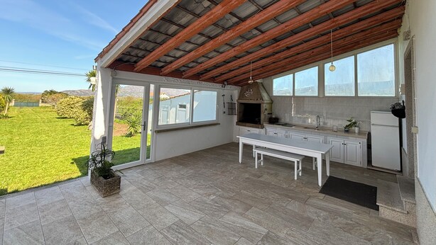 Un patio techado con área de cocina, que incluye un banco, gabinetes blancos y vistas al exterior.