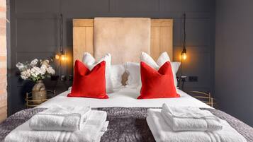 Una habitación de hotel moderna con una cama grande, dos almohadas rojas, toallas blancas y un florero con flores.