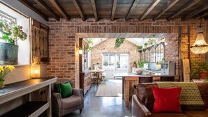 A rustic interior with exposed brick walls, a wooden ceiling, and a cozy seating area with leather sofas and cushions. - Boutique, three storey Georgian Town House, ground floor apartment with garden (Nantwich)