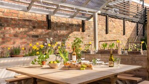 An outdoor dining area with a wooden table set for a meal, surrounded by potted plants and flowers. - Boutique, three storey Georgian Town House, ground floor apartment with garden (Nantwich)