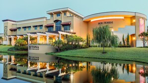 A large, modern building with a curved facade, a central entrance, and a reflection in a water feature. - Captivating Oceanview Suite w/ Balcony - Perfect for Family Fun | 2 Units (Daytona Beach)
