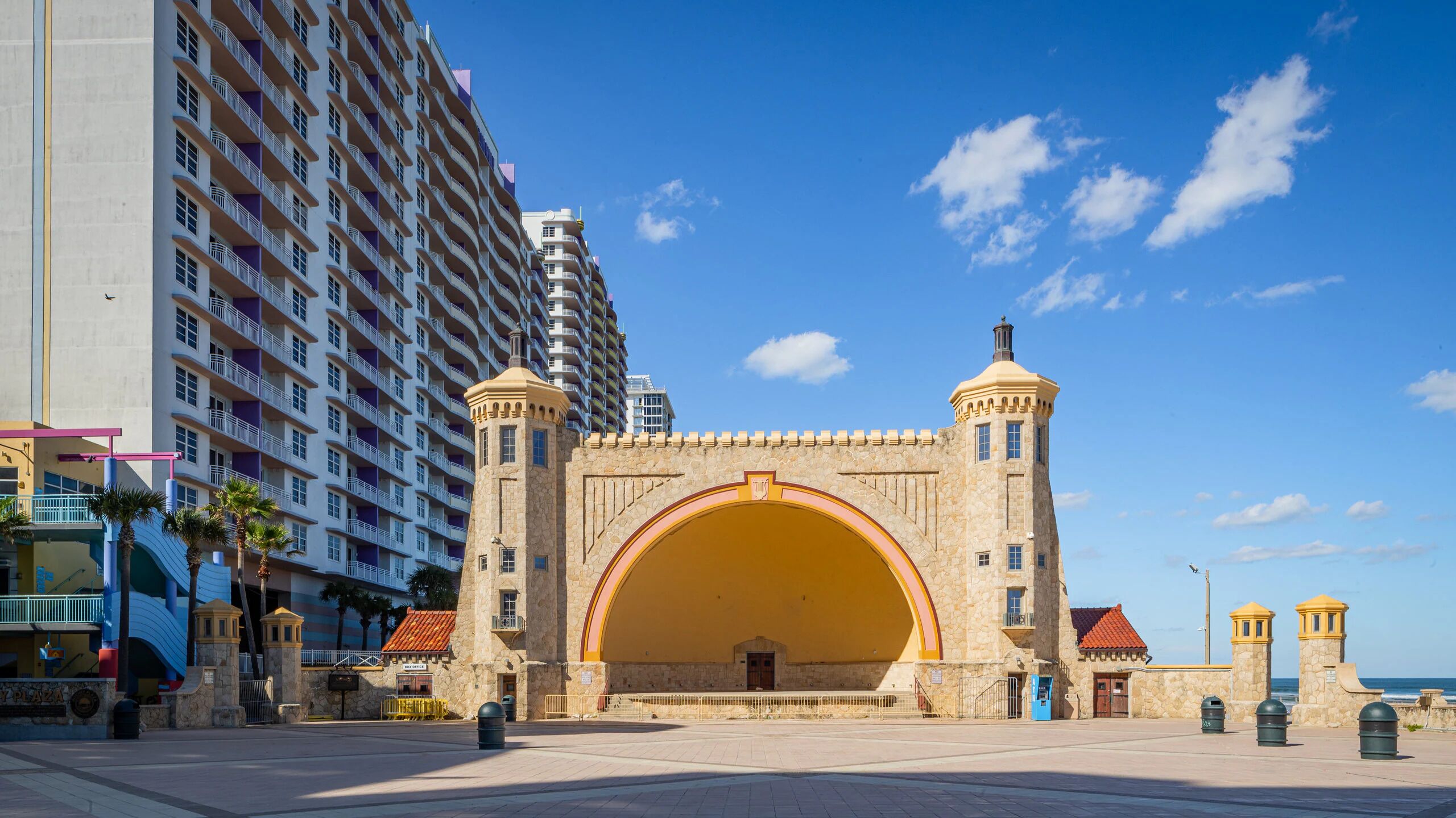 A historic stone archway with a large central arch, flanked by two towers, leading to a modern high-rise hotel.