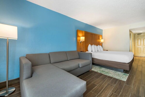 Une chambre d’hôtel avec un canapé gris, un lit avec une literie blanche et un mur d’accent bleu.