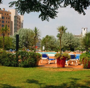 A poolside area with lounge chairs, a swimming pool, and surrounding greenery.