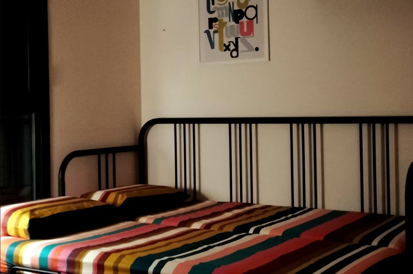 A bed with a striped bedspread, a black metal headboard, and a wall-mounted picture of letters.