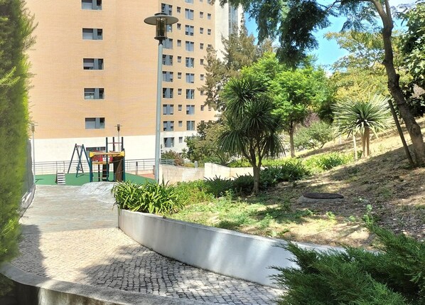 A pathway leading to a playground with a metal fence and a building in the background.
