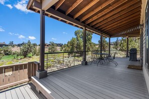Une terrasse extérieure couverte, dotée d’une table et de chaises, qui offre une vue sur un espace paysager agrémenté d’arbres et sur des maisons situées au loin.