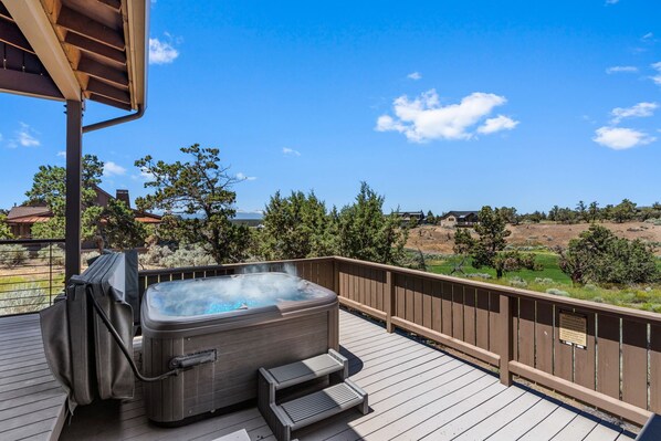 Un bain à remous sur une terrasse en bois, avec vue sur un espace paysager et des bâtiments situés au loin.