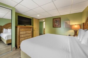 A hotel room with a large bed, a television, a wooden dresser, and a painting on the wall.