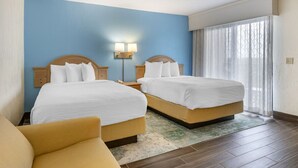 Habitación de hotel con dos camas, una mesita de noche, una lámpara y un ventanal con cortinas.