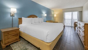 A hotel room with a large bed, wooden nightstands, a dresser, and a window with curtains.