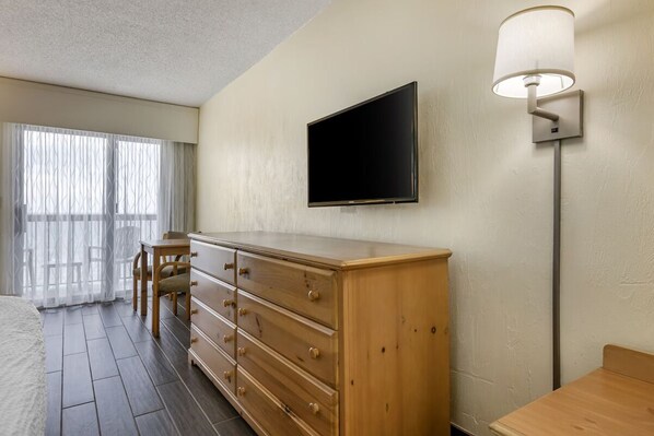 Hotelkamer met een houten dressoir, een flatscreen televisie aan de muur, een bureau met stoel en een raam met dunne gordijnen.