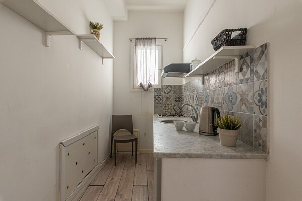A narrow kitchen with a wooden floor, a chair, a sink, a kettle, and a potted plant. - Real Umberto I - Suite 1 by Wonderful Italy (Palermo)