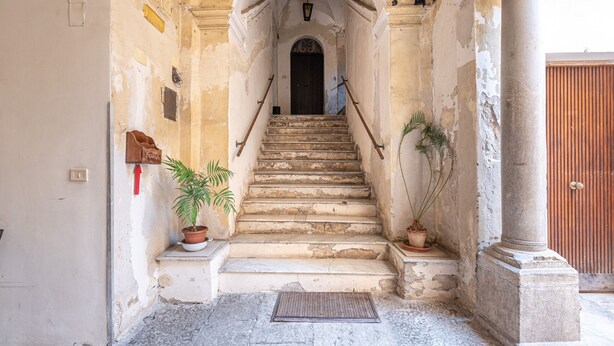 A staircase leading to a dark doorway, flanked by potted plants and a wooden mailbox. - Real Umberto I - Suite 1 by Wonderful Italy (Palermo)