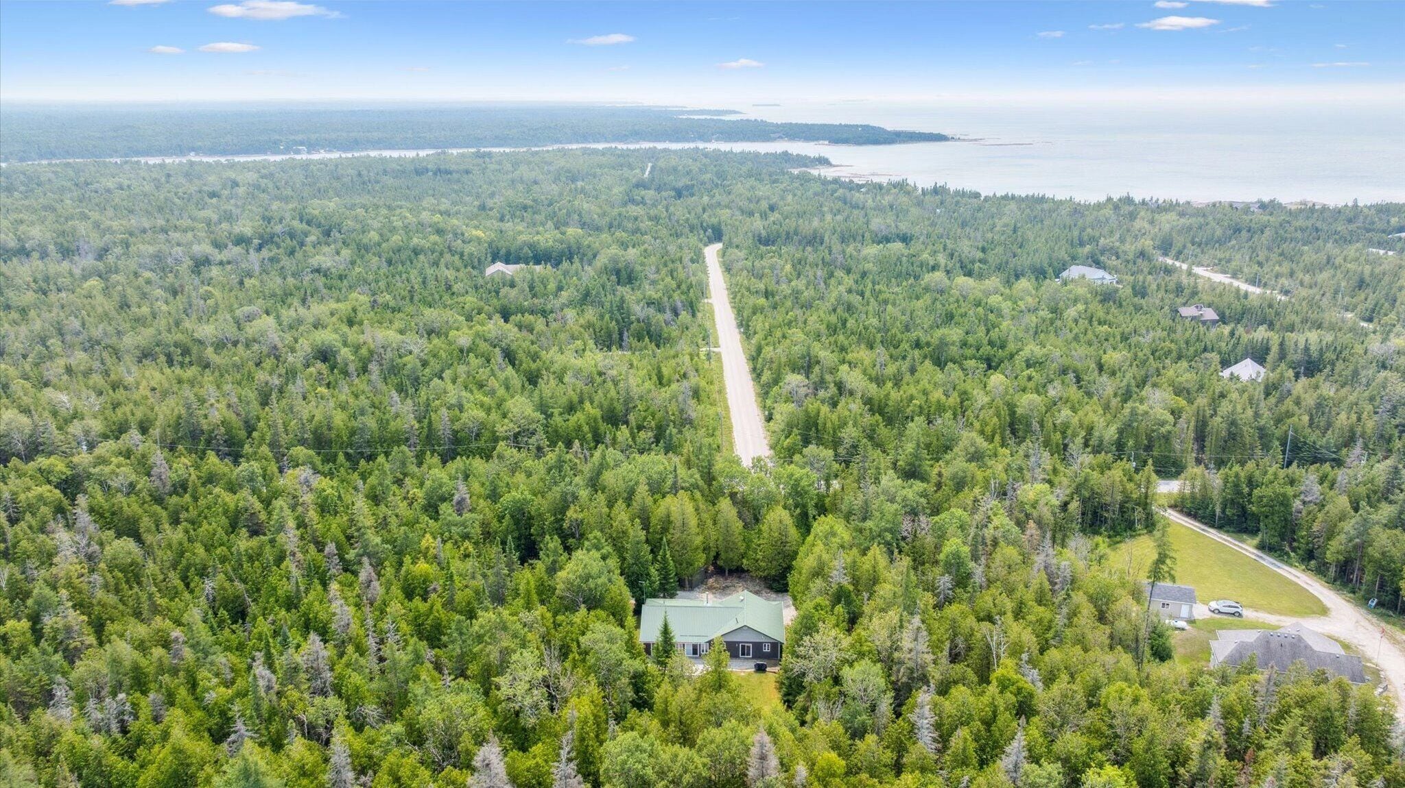Vista aérea de una zona boscosa con un camino que conduce a una casa de techo verde.
