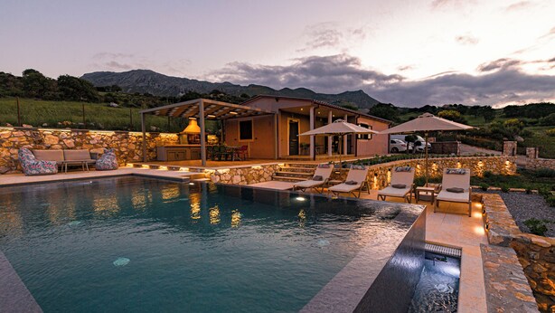 A pool area with lounge chairs and a covered seating area, surrounded by stone walls and a mountainous backdrop. - Kera Koxare Luxury Villa, Private Pool and Panoramic Mountain Views (Koxare Agiou Vasileiou)
