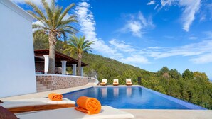 Un espace aménagé au bord de la piscine, avec des chaises longues et des serviettes, un mur en pierre et une vue sur une colline boisée.
