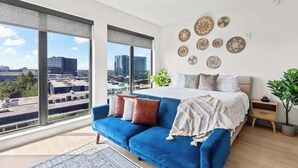 A modern bedroom with a large bed, a blue sofa, and a city view. - Skyline View Serene Oasis (Atlanta)
