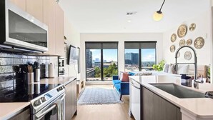 A modern kitchen with a large window, a built-in oven, and a dining area with a blue sofa. - Skyline View Serene Oasis (Atlanta)
